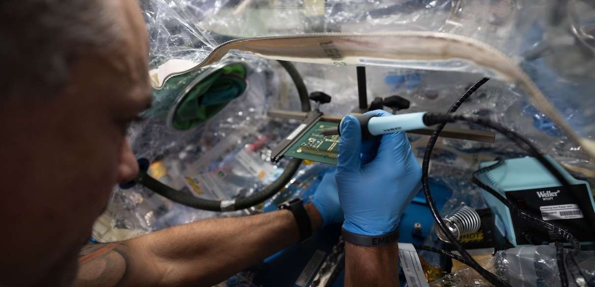 El astronauta de la NASA Anil Menon utiliza una técnica de soldadura sin plomo para soldar componentes en una placa de circuito